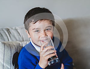 Portrait schoolboy drinking soda or soft drink with glass,Child enjoying cold fizzy dink after back from school,Kid relaxing at