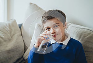 Portrait schoolboy drinking soda or soft drink with glass,Child enjoying cold fizzy dink while watching TV after back from school,