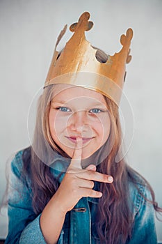 Portrait of schoolgirl with colored hair wearing golden crown and showing silence gesture.