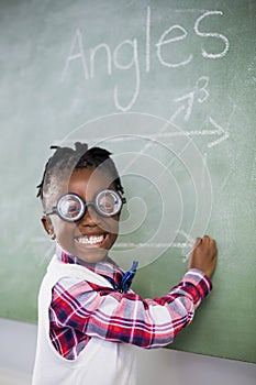 Portrait of schoolgirl doing mathematics on chalkboard in classroom