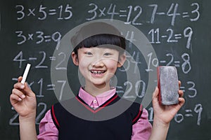 Portrait of schoolgirl in front of blackboard holding chalk and eraser