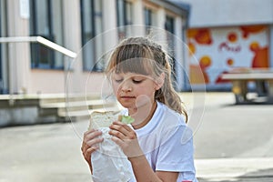 Portrait of a schoolgirl girl who eats her lunch, a snack in the school yard. Food for children in educational institutions,