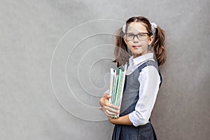 Portrait of a schoolgirl on a gray background with textbooks in her hands