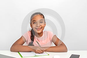 Portrait of the schoolgirl siting at the table  indoors and doing her homework