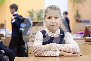 Portrait of schoolgirl sitting at desk in classroom at recess while other schoolkids playing