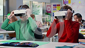 Portrait of schoolkids sitting at desk and putting on vr headset in classroom