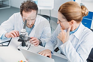 portrait of scientific researchers in white coats working together at workplace with microscope