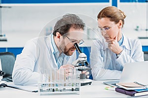 portrait of scientific researchers in white coats working together at workplace with microscope