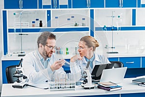 portrait of scientific researchers in white coats at workplace with flasks microscopes and laptop