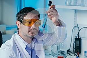 Portrait of a scientist working in the lab examines a test tube with liquid.