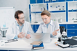 portrait of scientists in lab coats and eyeglasses working together at workplace with laptop