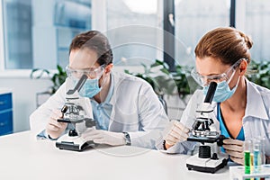 portrait of scientists in medical masks and gloves looking through microscopes on regents