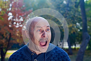 Portrait of a screaming bald man in a blue sweater