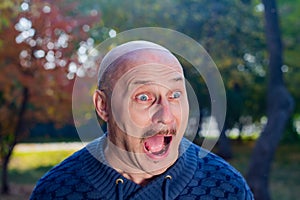 Portrait of a screaming bald man in a blue sweater