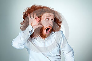 Portrait of screaming young man with long red hair and shocked facial expression on gray background