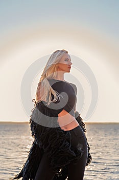 Portrait of a seductive blonde pensively standing in black clothes with a sunset lake on a background