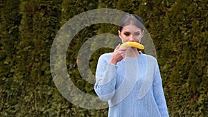 Portrait seductive young woman with dark hair and red lips in blue jacket pulls out banana and applies it imitating mustache