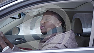 Portrait of self-confident african american woman sitting in the car chewing gum close up. Beautiful woman driving in