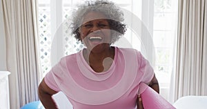 Portrait of senior african american woman holding yoga mat smiling at home