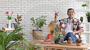A portrait of a senior Asian man gardener poses with happy in planting corner at home. He points finger to high position