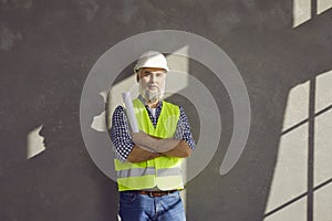 Senior builder, foreman, construction engineer or architect standing by grey house wall