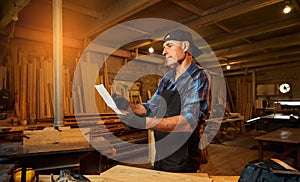 Portrait of a senior carpenter looking at blueprints plans  to make a piece of furniture in the carpentry workshop