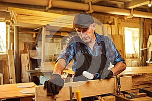 Portrait of a senior carpenter in uniform gluing wooden bars with hand pressures at the carpentry manufacturing