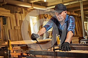 Portrait of a senior carpenter in uniform gluing wooden bars with hand pressures at the carpentry manufacturing