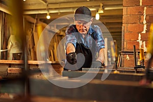 Portrait of a senior carpenter in uniform gluing wooden bars with hand pressures at the carpentry manufacturing