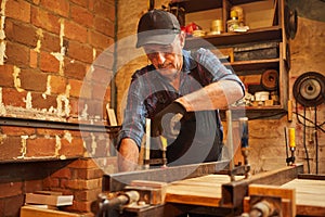 Portrait of a senior carpenter in uniform gluing wooden bars with hand pressures at the carpentry manufacturing