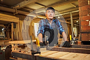 Portrait of a senior carpenter in uniform gluing wooden bars with hand pressures at the carpentry manufacturing
