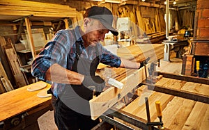 Portrait of a senior carpenter in uniform gluing wooden bars with hand pressures at the carpentry manufacturing