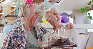 Portrait of senior caucasian couple holding cake and celebrating birthday at home