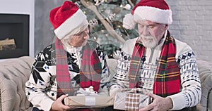 Portrait of senior Caucasian couple sitting with Christmas presents on sofa and thinking. Positive woman and man in red