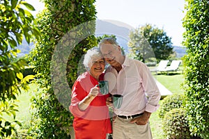 Portrait of senior caucasian couple smiling and holding mugs in sunny garden