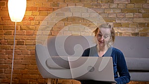 Portrait of senior caucasian lady sitting on floor and working with laptop with positive laughter in cozy home