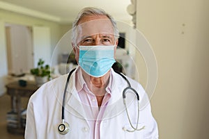 Portrait of senior caucasian male doctor wearing face mask looking at camera