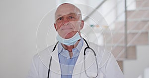 Portrait of senior caucasian male doctor wearing face mask looking at camera and smiling