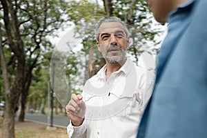 Portrait of a senior caucasian man giving advice and suggestion to his son while walking and discussion problem in the park,
