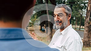 Portrait of a senior caucasian man giving advice and suggestion to his son while walking and discussion problem in the park,