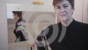 Portrait of senior caucasian woman posing in front of big mirror, turning to camera and smiling. Happy elegant lady