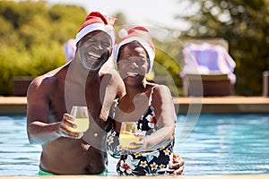 Portrait Of Senior Couple On Christmas Holiday In Swimming Pool Wearing Santa Hats