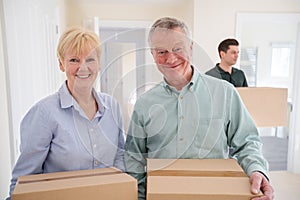 Portrait Of Senior Couple Downsizing In Retirement Carrying Boxes Into New Home On Moving Day With Removal Man Helping