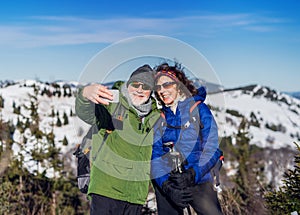 Senior couple hikers standing in snow-covered winter nature, taking selfie.