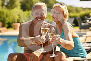 Portrait Of Senior Couple On Holiday In Swimming Costumes Drinking Champagne By Hotel Swimming Pool