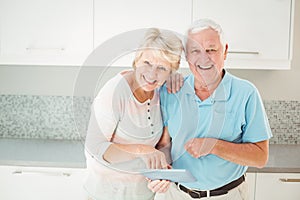 Portrait of senior couple laughing with tablet in kitchen