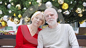 Portrait of senior couple near decorated Christmas tree at mall. Happy family sitting and smiling