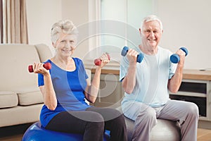 Portrait of senior couple sitting on fitness balls with dumbbells