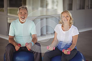 Portrait of senior couple sitting on fitness balls with dumbbells