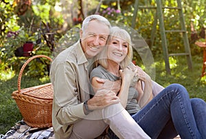 Portrait of senior couple sitting in garden and hugging, having picnic outdoors and smiling to camera